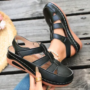 Detailansicht schwarzer Keilsandalen aus Leder mit weißen Ziernähten und Klettverschluss.
