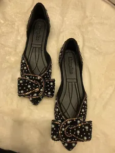 Gedetailleerd overzicht van zwarte platte schoenen met een strik van parels en strass.