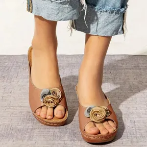 Primer plano de sandalias con cuña marrones con adornos florales usadas por una modelo