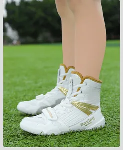 Detail shot of white high-top boxing shoes with gold accents worn on green grass