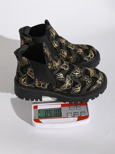 Medición del peso de botines Chelsea negros con estampado de mariposas doradas en báscula.