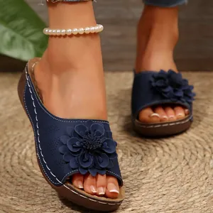 Primer plano de elegantes sandalias con cuña azul marino y una gran flor decorativa.