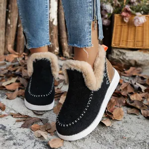Primer plano de botas de nieve negras para mujer con forro de felpa y suela blanca gruesa.