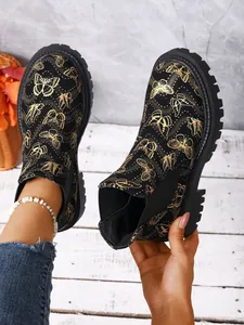 Detalle de botines Chelsea negros con elegantes estampados de mariposas doradas