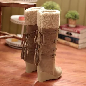 Detalle de botas de nieve con cuña, cordones traseros y borlas decorativas para el invierno.