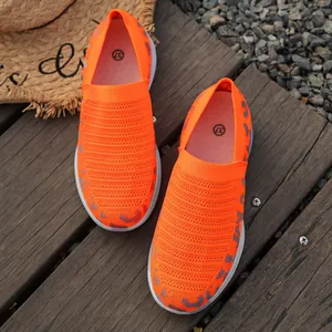 Gedetailleerd bovenaanzicht van oranje fly-knit dames instappers op houten ondergrond.