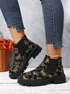 Primer plano de botas Chelsea negras con estampado de mariposas doradas en modelo.