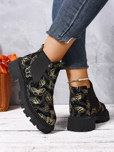 Detalle de botines Chelsea estampados con mariposas doradas y suela dentada.