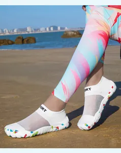 Detailed view of breathable white mesh water shoes with colorful soles on a sandy beach.
