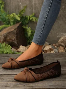 Detail view of brown pointed-toe knit flats with bow decoration on wooden floor.