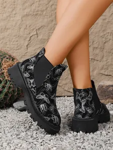 Vista detallada de botines Chelsea negros con estampado de mariposas y suela gruesa