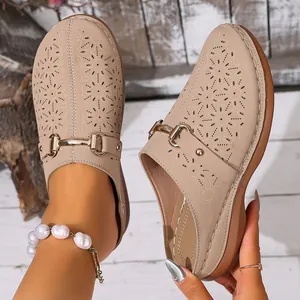 Close-up detail of beige hollow platform mules with gold chain and floral patterns.