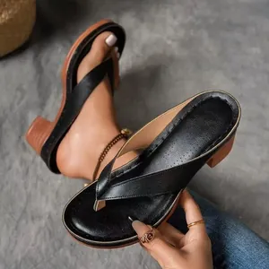 Nahaufnahme von schwarzen Zehentrenner-Sandalen mit braunem Keilabsatz in der Hand