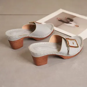 Detailed view of grey high-heeled mule sandals with a gold buckle and wooden heel.
