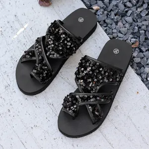 Gros plan de sandales pour femmes à paillettes noires sur un sol texturé