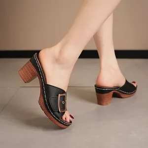 Detailed side view of black mule sandals featuring a gold buckle and chunky wood-textured heel.
