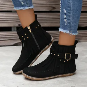 Primer plano de botines negros con flecos y tachuelas doradas sobre una modelo