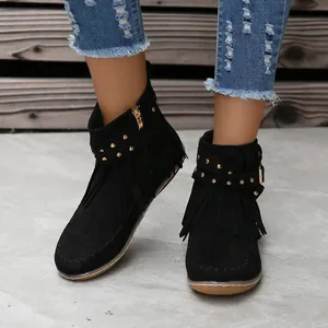Detalle de botines de ante negro con flecos y tachuelas doradas con vaqueros azules