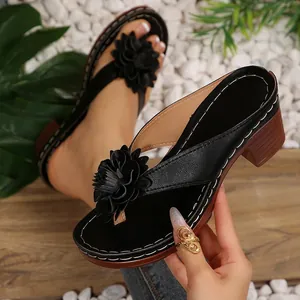 Detail view of black wedge thong sandals with a large decorative flower and white stitching