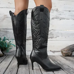 Vue détaillée de bottes de cowboy noires à talons hauts avec broderie sur fond bois rustique