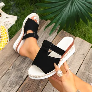 Black platform wedge sandals with straw-textured sole on rustic wooden background.