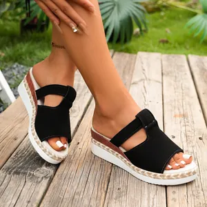 Close-up of black platform wedge sandals with woven rope detail on wooden floor
