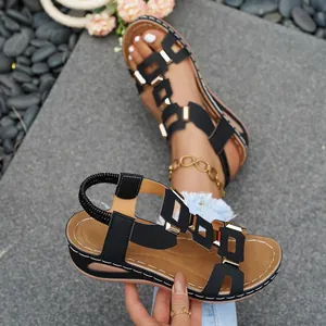 Detail view of black wedge sandals with gold metal buckles and elastic straps