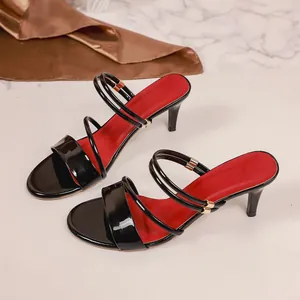 Detail of black patent leather high-heeled sandals with red insoles and gold buckles.
