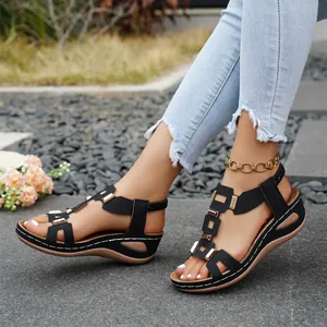 Close-up view of women's black wedge sandals with metal buckles worn outdoors