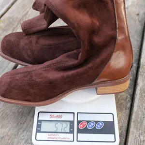 Detailed close-up view of brown women's tall boots on a scale showing 572g weight.
