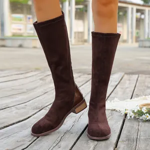 Detailed view of brown suede knee-high boots with low heel on wooden floor