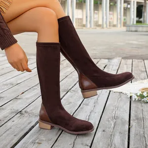 Close-up detail of brown suede knee-high boots with square toe on a wooden background.