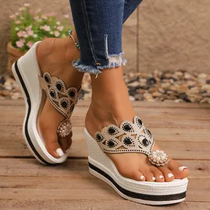 Primer plano de chanclas con cuña decoradas con pedrería negra y detalle de flor de perla.