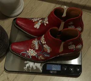 Close-up view of red embroidered western boots on a scale showing a weight of 808 grams