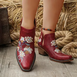 Vintage red Western boots with floral embroidery and chunky heels shown in a rustic setting.