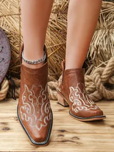 Detailed view of brown retro ankle boots with white floral embroidery and chunky heel.