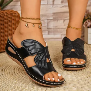 Detail of black butterfly wing sandals with contrast stitching and wedge sole on straw mat
