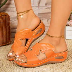 Detail view of orange wedge slippers with butterfly wing straps and contrast stitching