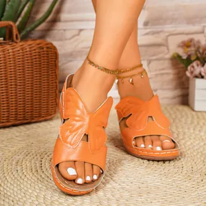 Detail of orange butterfly wedge sandals with open-toe design on a braided mat