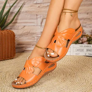 Detail view showing orange butterfly open-toe wedge sandals on a person outdoors.