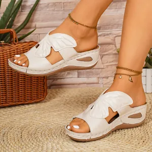Close-up of elegant leaf-patterned off-white wedge sandals for women worn with anklets