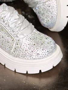 Close-up detail of white platform sneakers with shimmering AB rhinestones and satin laces
