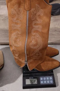 Close-up detail of a brown suede embroidered cowboy boot being weighed on a scale