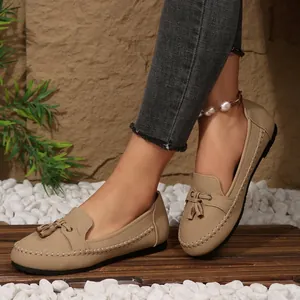 Women's beige flat loafers with tassels and stitching detail in an outdoor setting