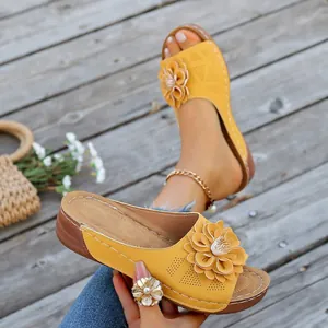 Close-up of yellow wedge sandals featuring a large decorative flower and perforated strap