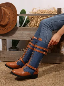 Detail view of denim and leather spliced tall boots with buckle straps and lace-up front