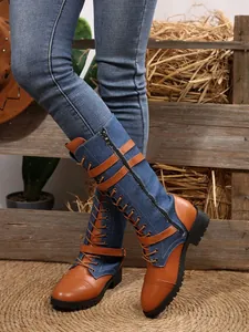 Detail of denim and tan leather knee-high boots with buckle straps and laces.