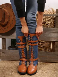 Detail view of denim and brown leather patchwork knee-high boots with buckle straps.