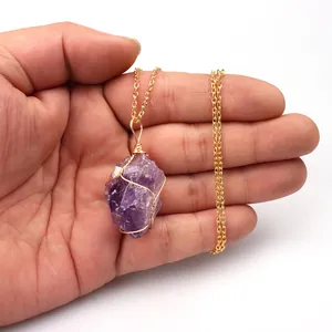 Detailed view of handmade amethyst crystal pendant with gold wire wrap on a hand