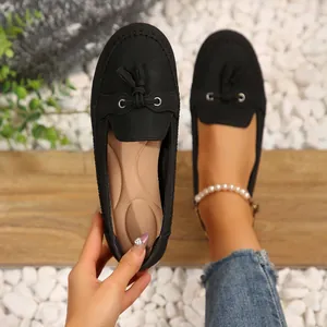 Mocassins noirs pour femmes avec pompons portés et tenus sur un fond de galets blancs